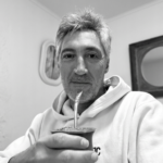Hombre con sudadera clara tomando mate en blanco y negro en un ambiente cálido de estudio