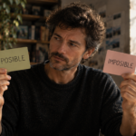 Hombre pensativo sostiene dos tarjetas, una con la palabra «POSIBLE» y otra con «IMPOSIBLE», mientras mira hacia ambos lados.